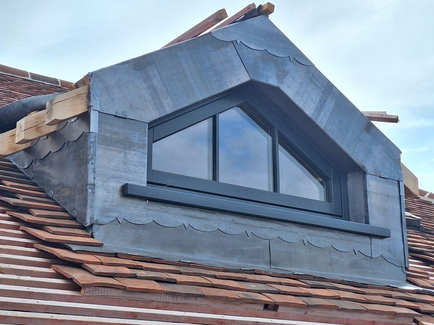 Lead-clad dormer with a pitched window and hand-cut scalloped lead edging, set into a clay tile roof