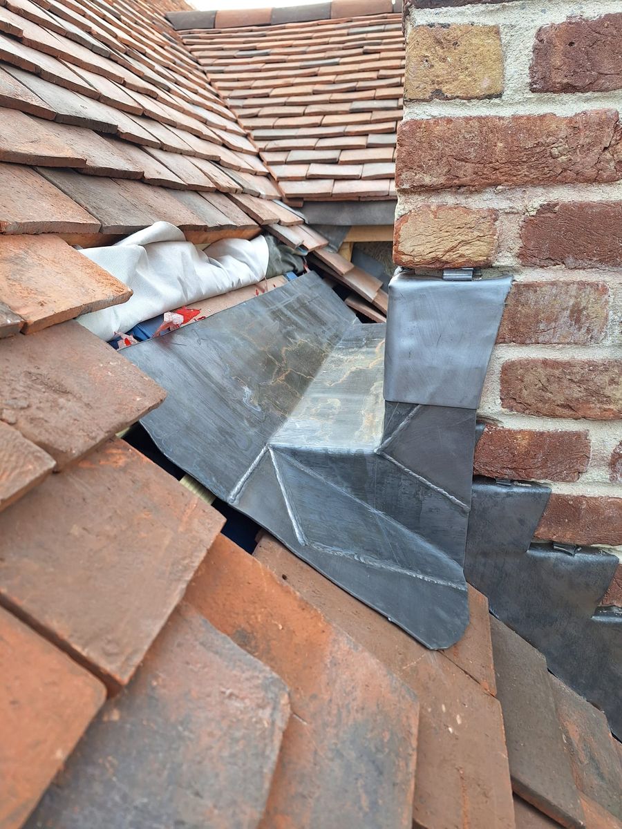 Welded lead gutter and stepped lead flashing where a clay tile roof meets brickwork